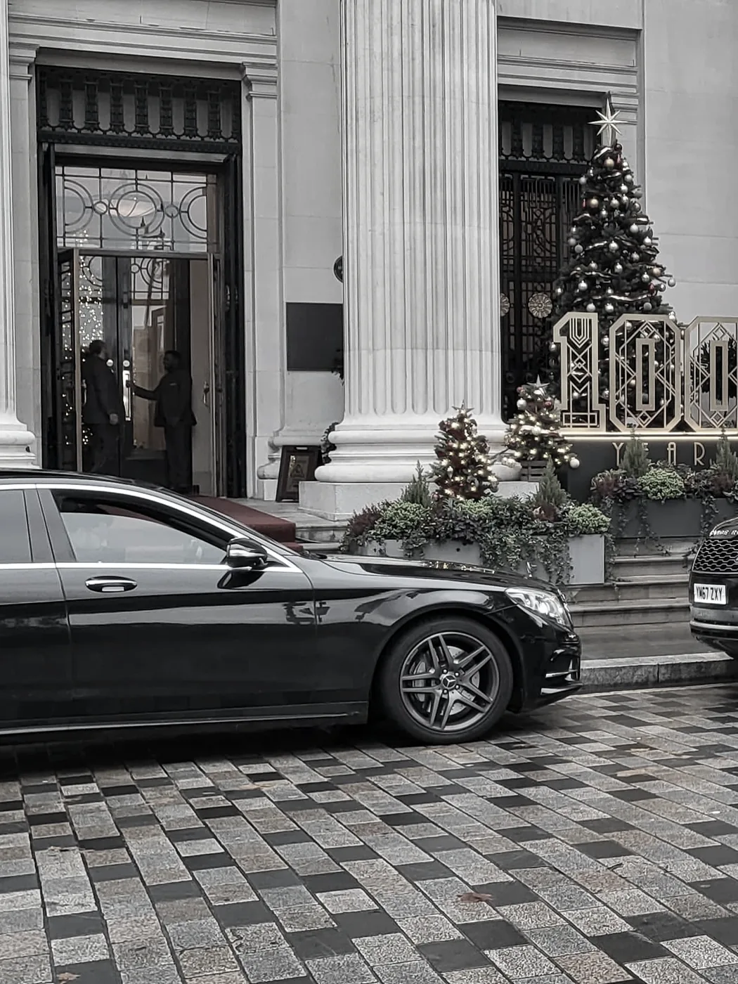 A grand columned London entrance at Christmas, a private car waiting at the door.